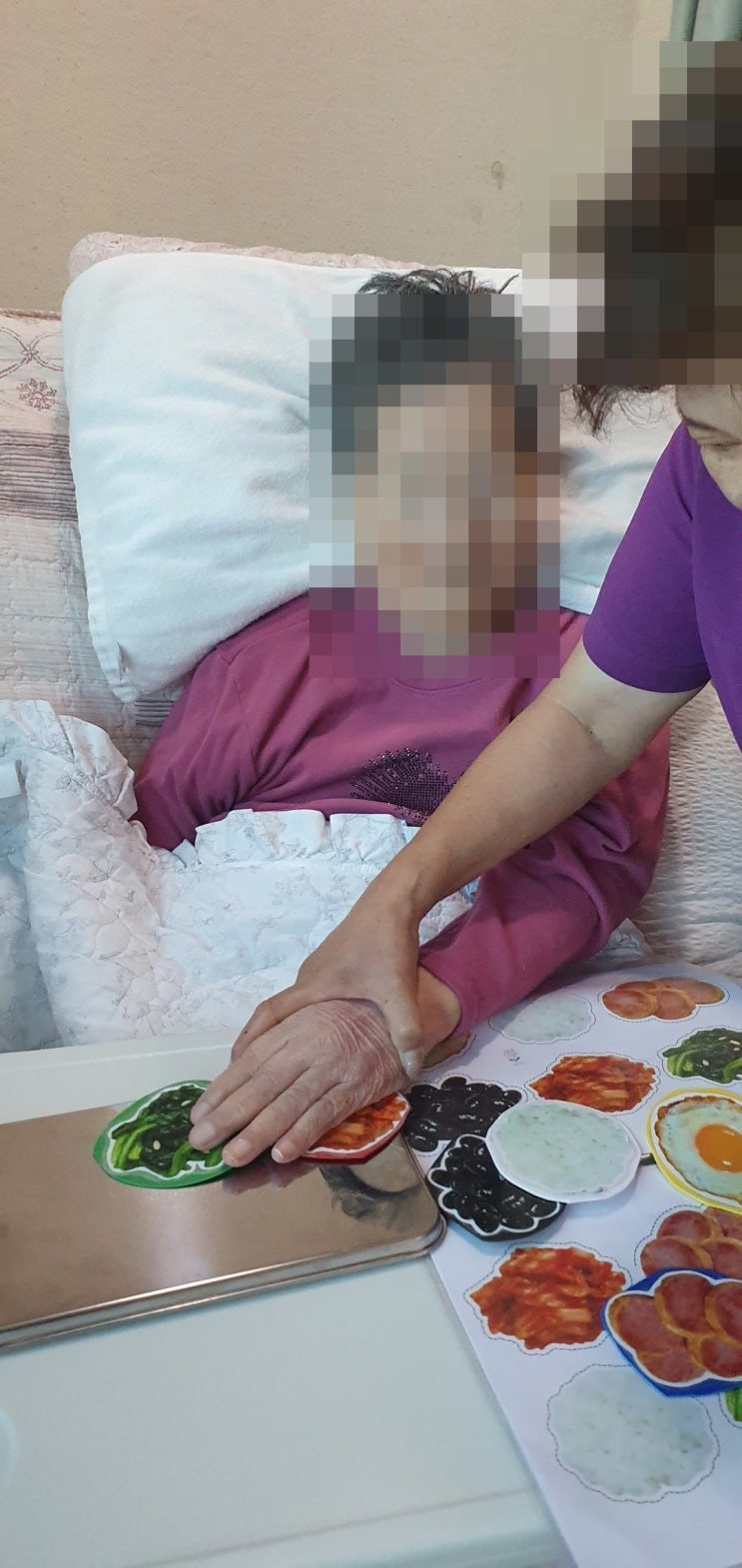 침상에서 선생님 도움을 받아 반찬 모형을 만져 보시는 어르신
