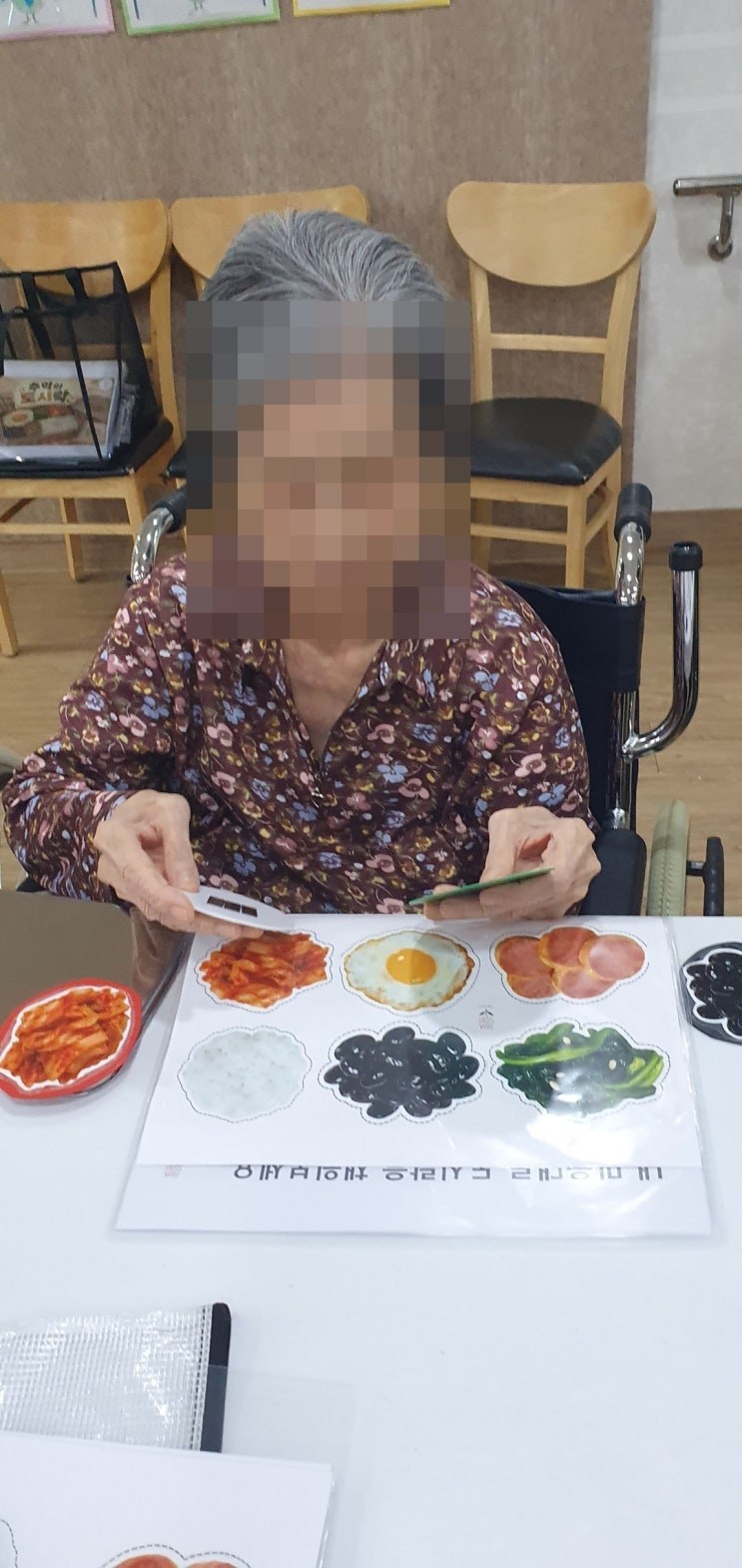 완성해 가는 도시락 워크지를 살펴보시는 어르신
