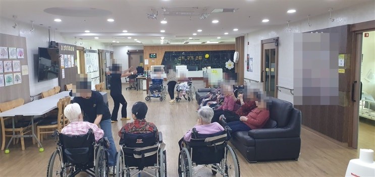 청주 성지요양원 거실에서 휠체어에 앉은 어르신들이 선생님과 함께 몸풀기를 하는 모습, 얼굴은 개인정보 보호를 위해 모자이크 처리