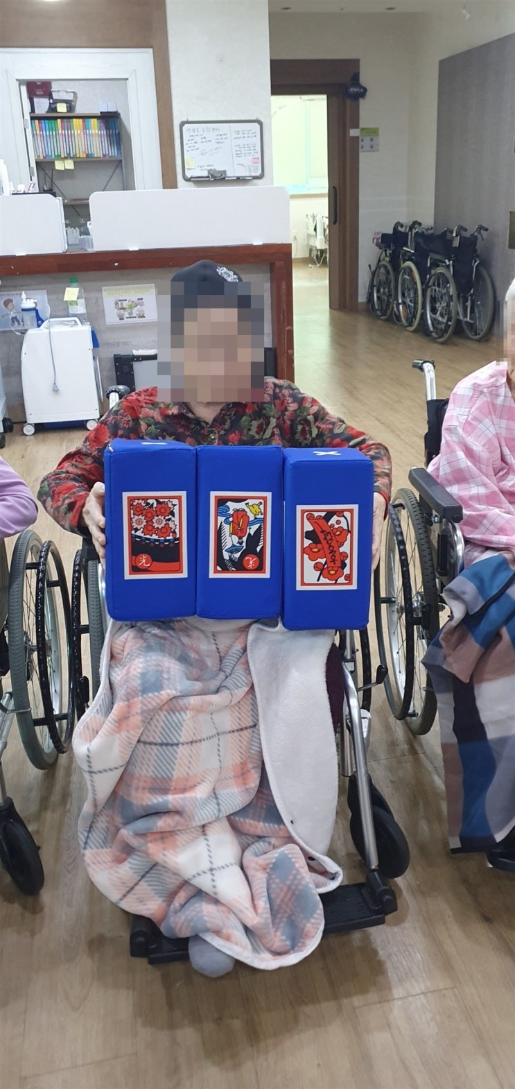 휠체어에 앉아 주사위 그림을 보여 주시는 어르신