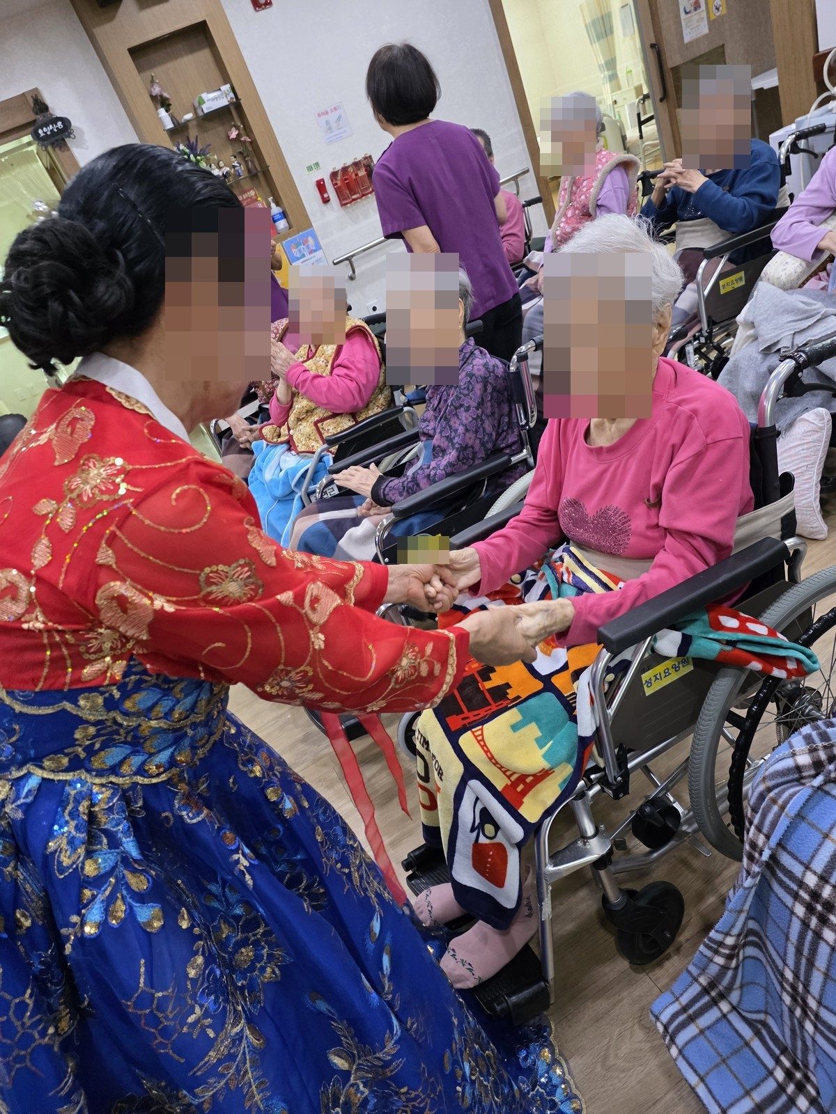 휠체어에 앉은 어르신의 손을 잡아 드리는 한복 차림 단원