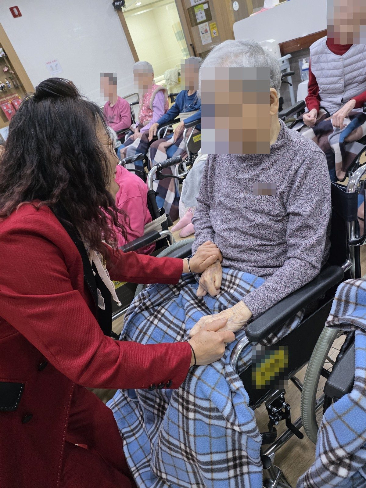어르신 곁에 앉아 손을 잡고 노래하는 봉사단 단원